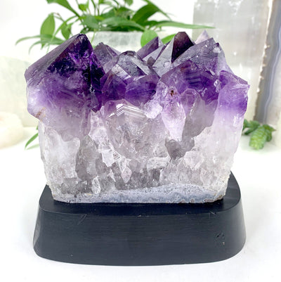 side view of Amethyst Cluster with Calcite Formations on Wood Base with decorations in the background