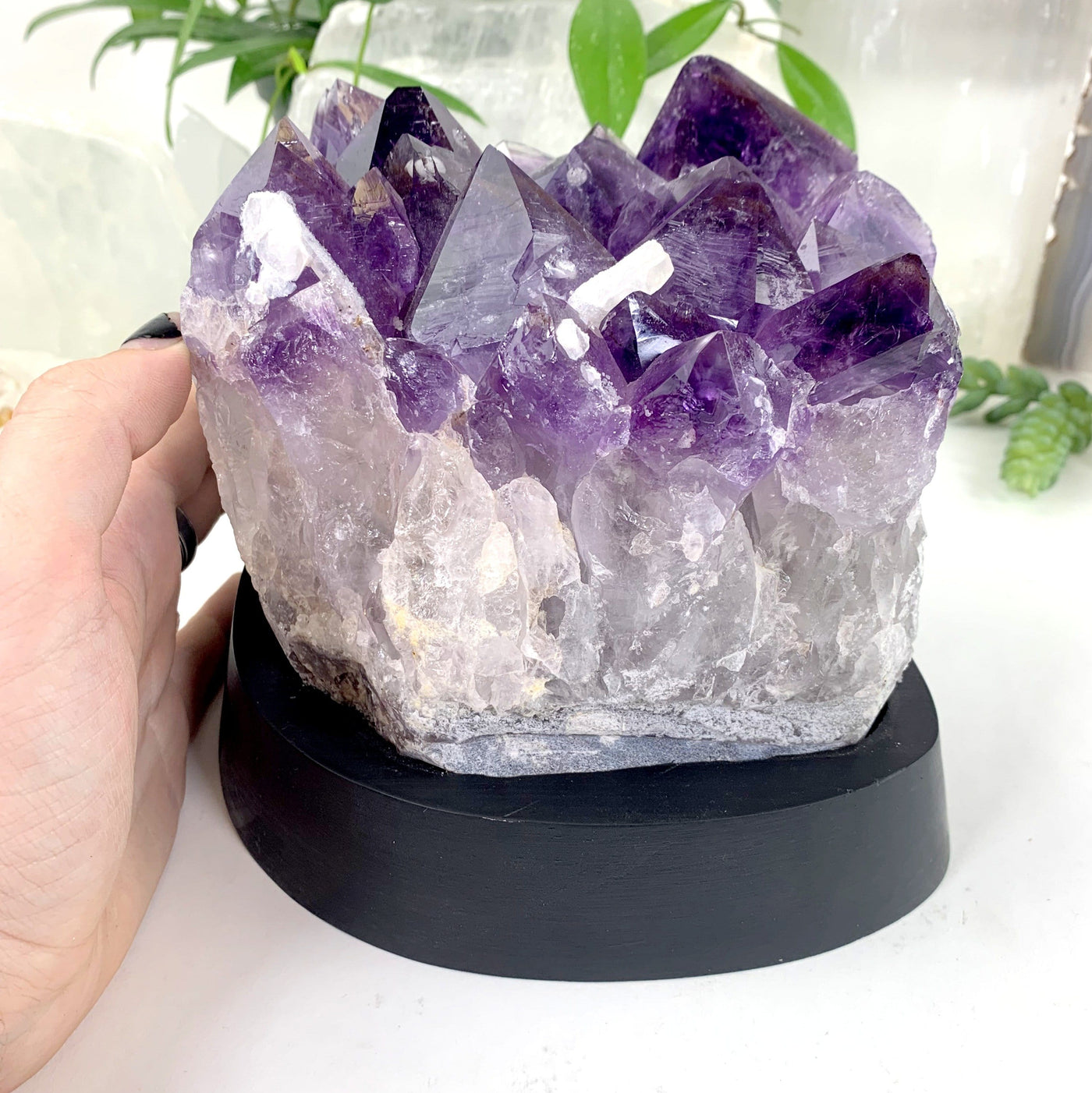 hand next to Amethyst Cluster with Calcite Formations on Wood Base with decorations in the background