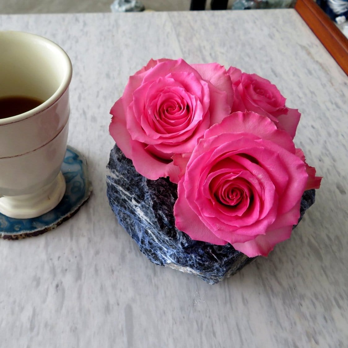 close up of one sodalite planter with three roses inside and a teacup next to it