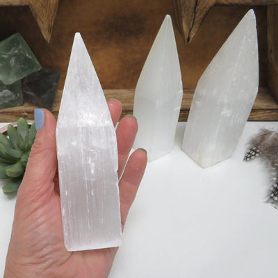 one selenite tower obelisk point in hand for size reference with others in background display
