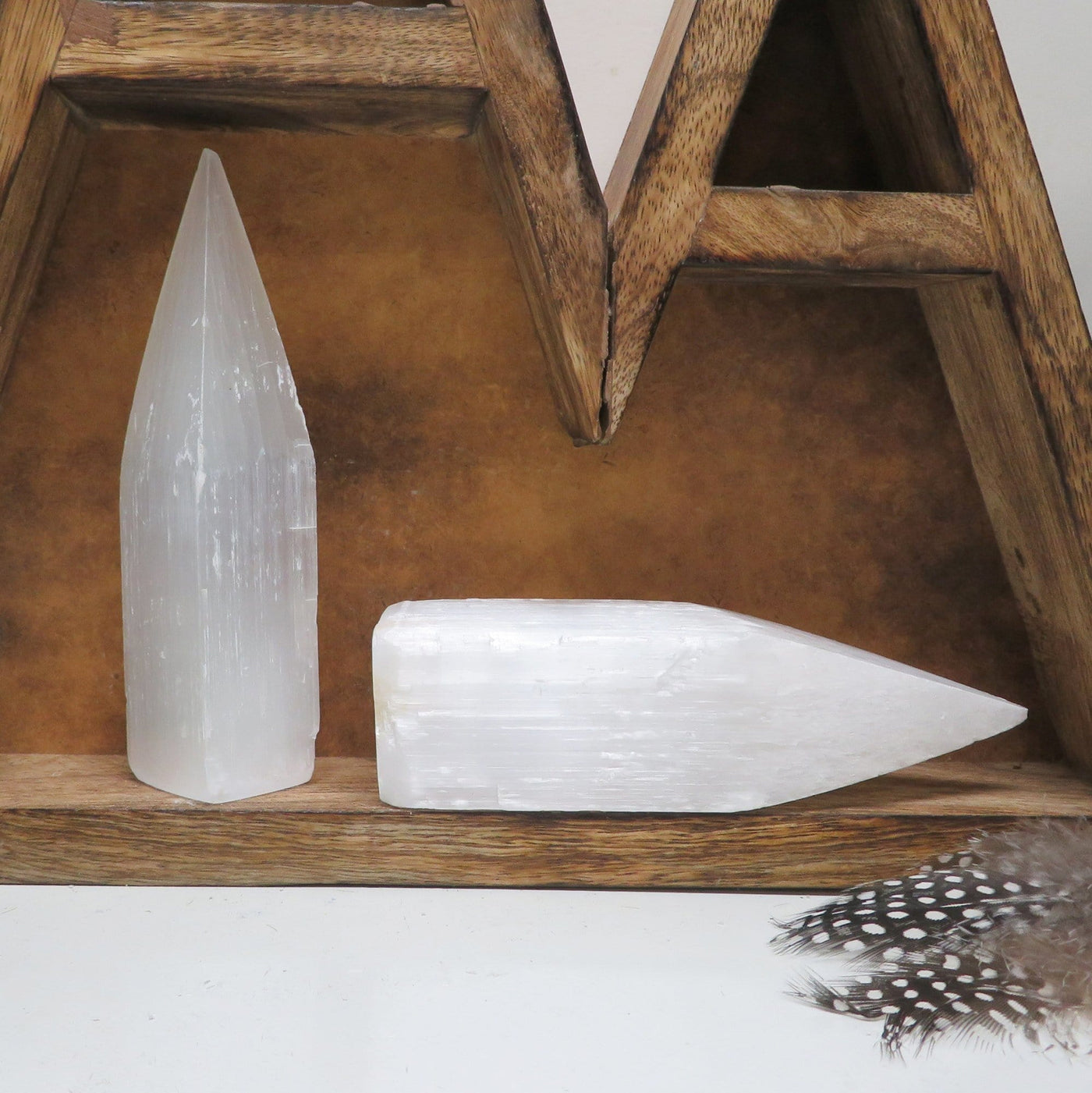 one selenite tower obelisk point on display with a second selenite tower obelisk point laying on its side