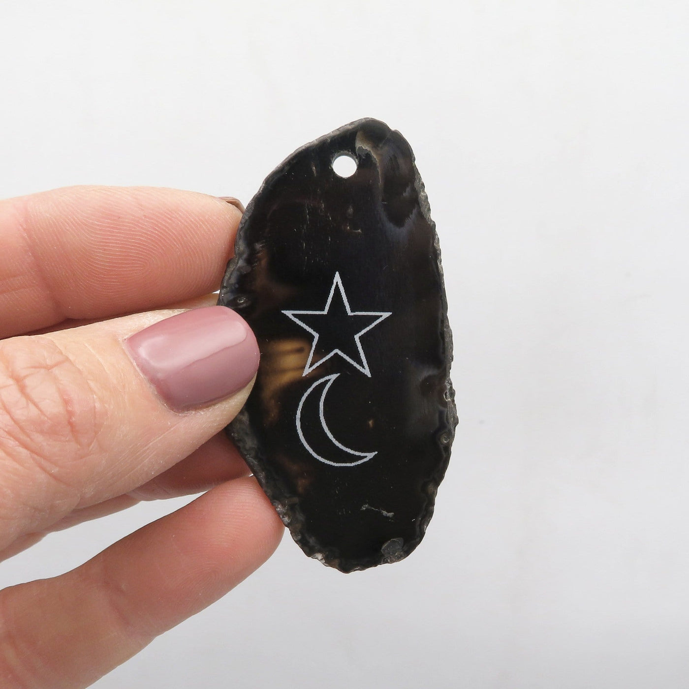 Picture of one black agate slice drilled, in hand for size reference.