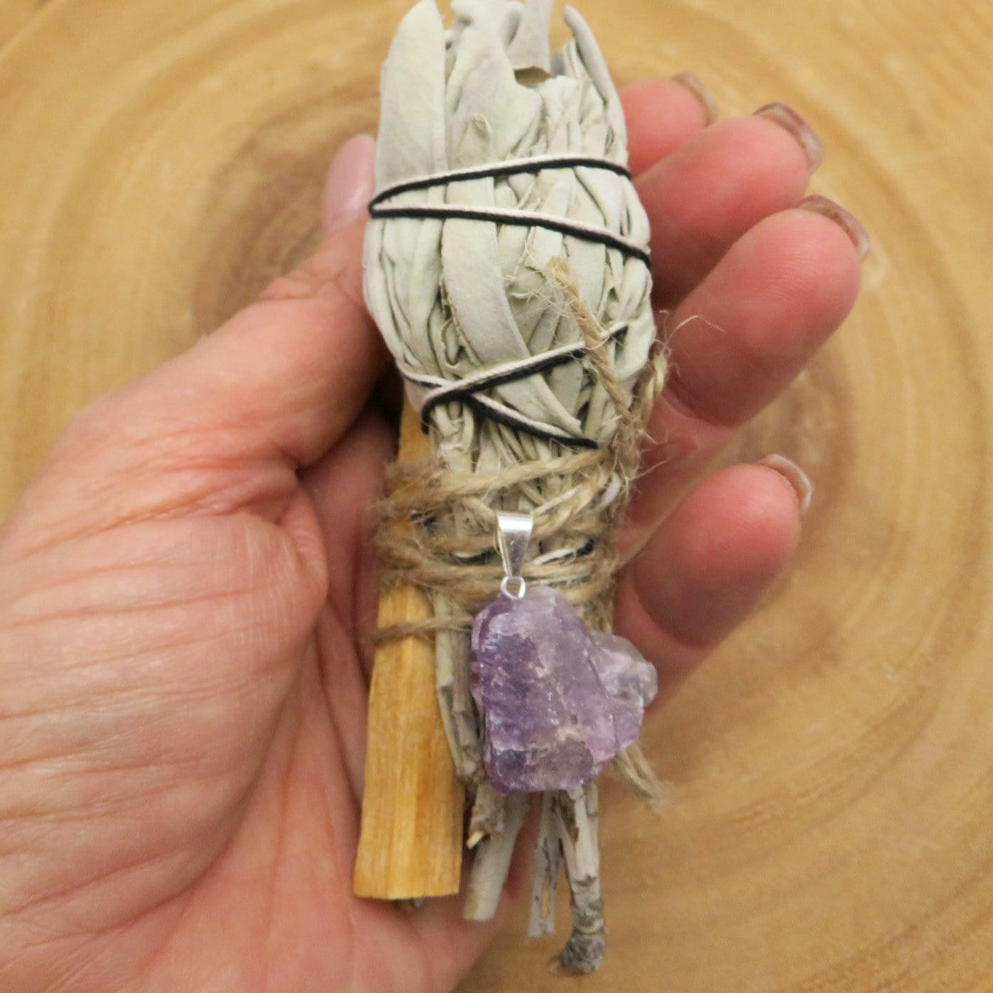 close up of sage palo santo bundle with amethyst pendant for size reference and possible variations