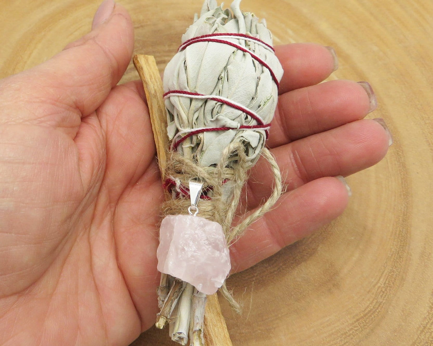 close up of sage palo santo bundle with rose quartz pendant for size reference and possible variations
