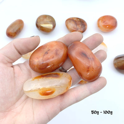 3 50gram to 100 gram carnelian stones in hand with a white background