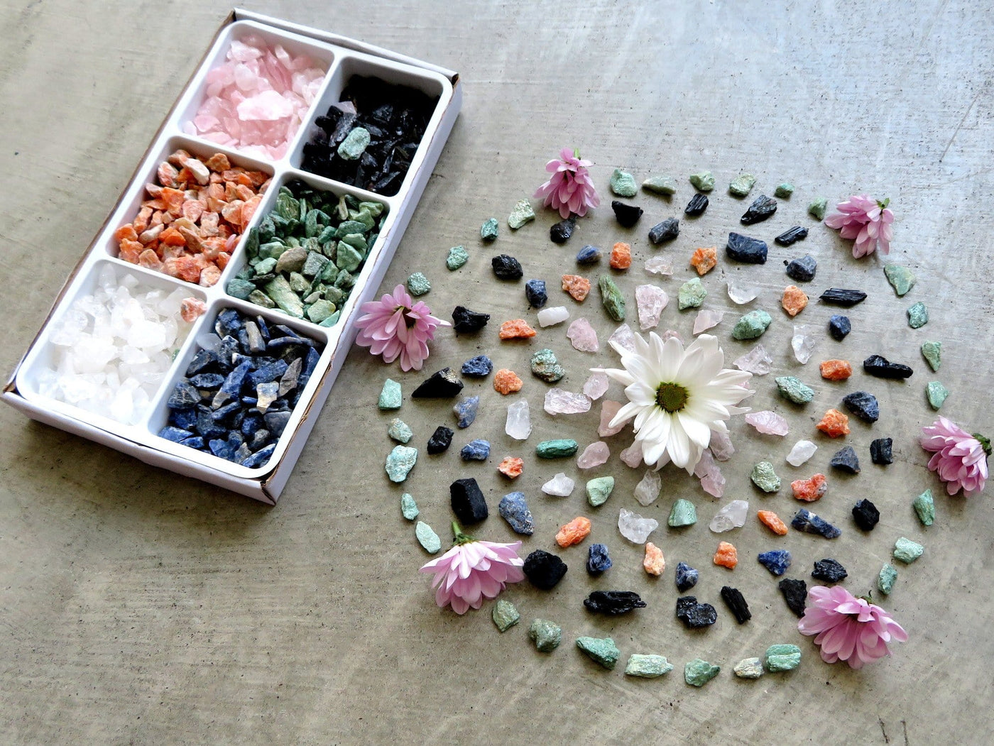 Box of crystals next to Rough Stone Mixed Set Crystal Grid with flowers