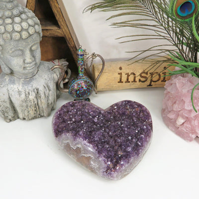 Large amethyst cluster heart on a white background with other crystals and decorations around it.