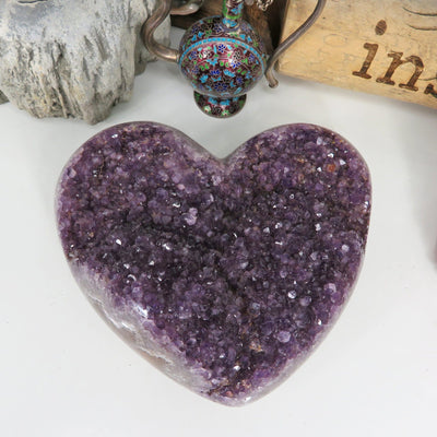 Large amethyst cluster heart on a white background with other crystals and decorations around it.