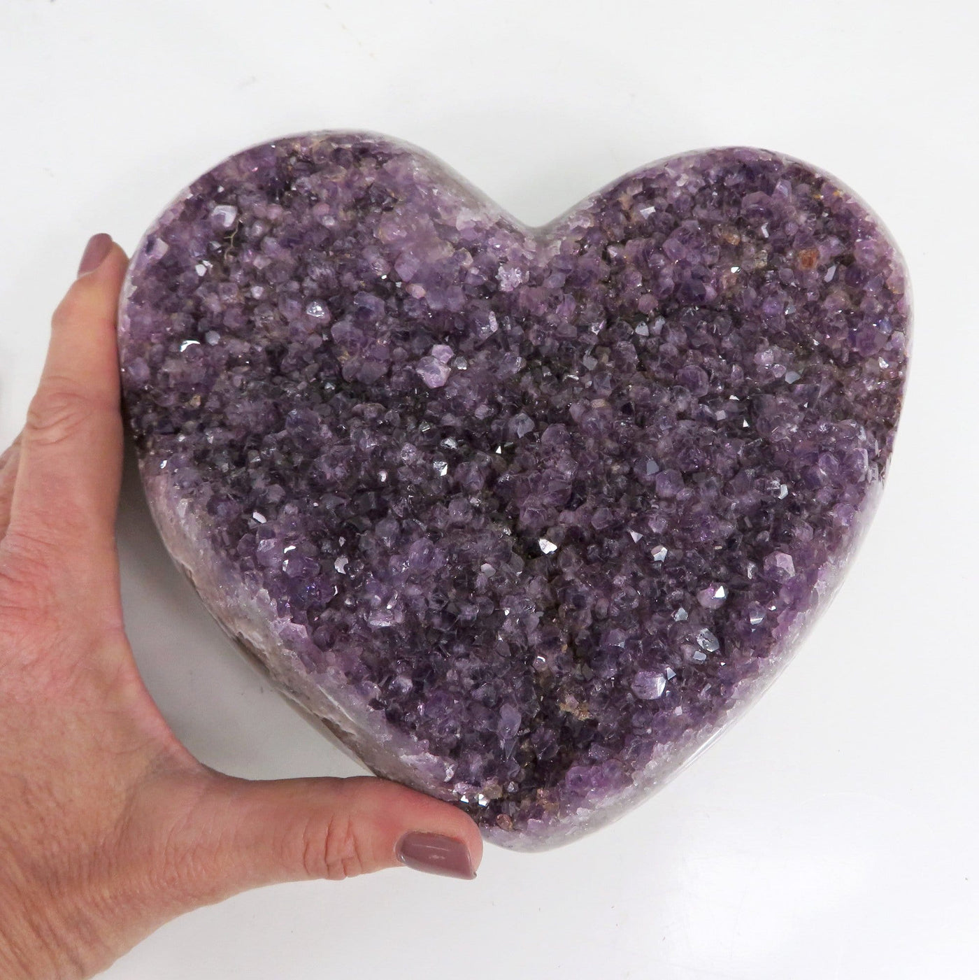 Large amethyst heart cluster with a woman's hand next to it on a white background.