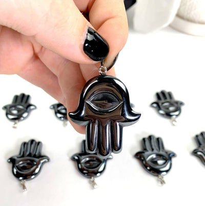 one single hematite hamsa hand all seeing eye pendant being held for size reference