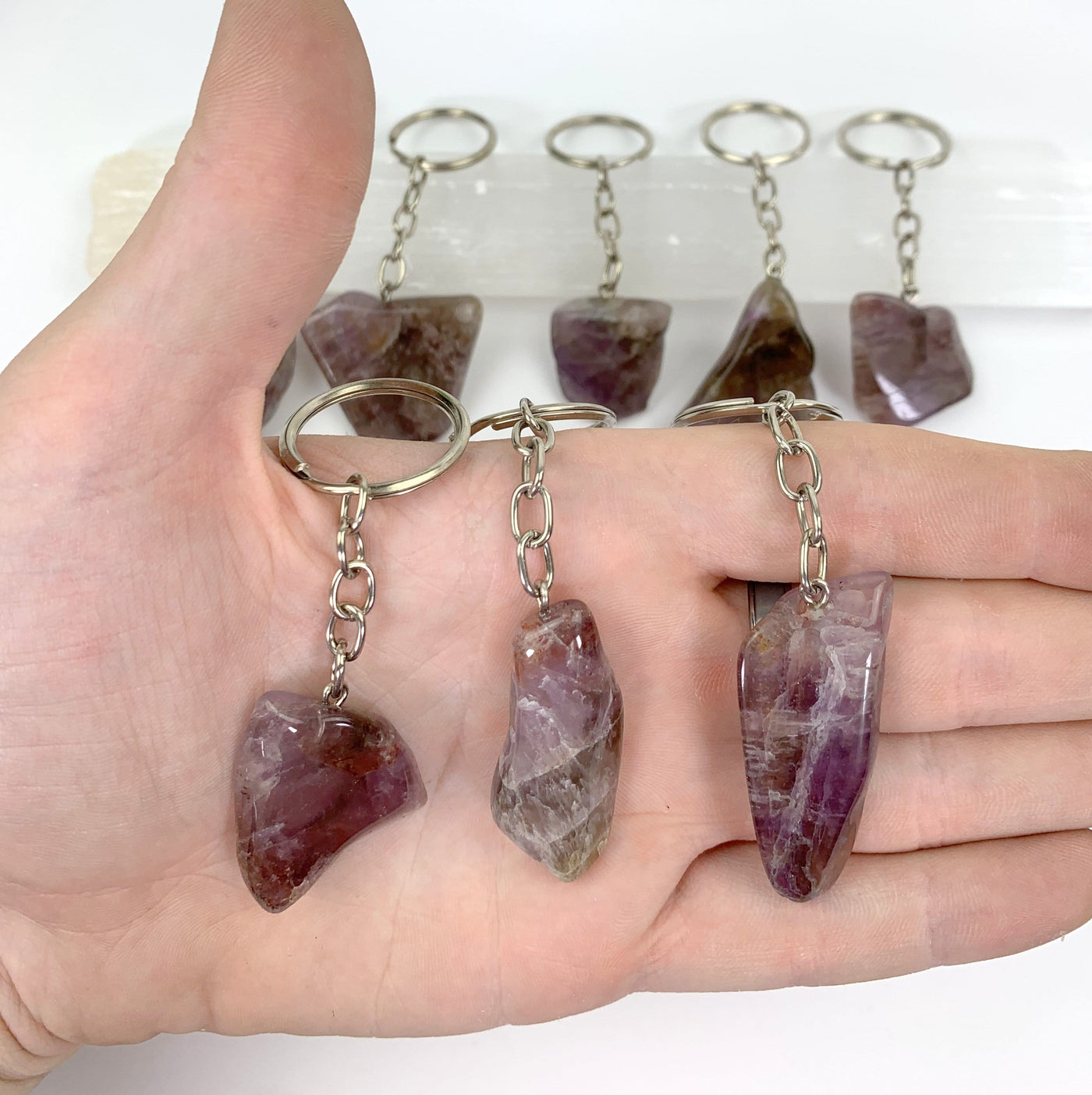 three seven mineral amethyst slab keychains in hand for size reference with others in background