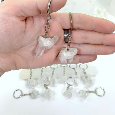 two Crystal Clusters Keychains  in a hand with others behind on a table