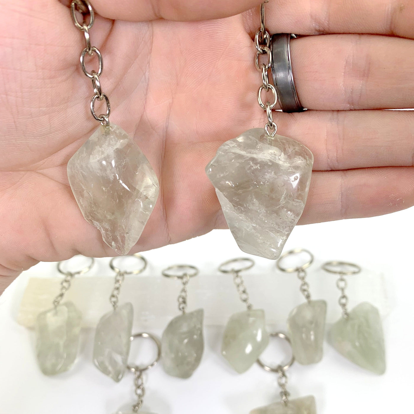hand holding up 2 prasiolite keychains with others blurred in the background