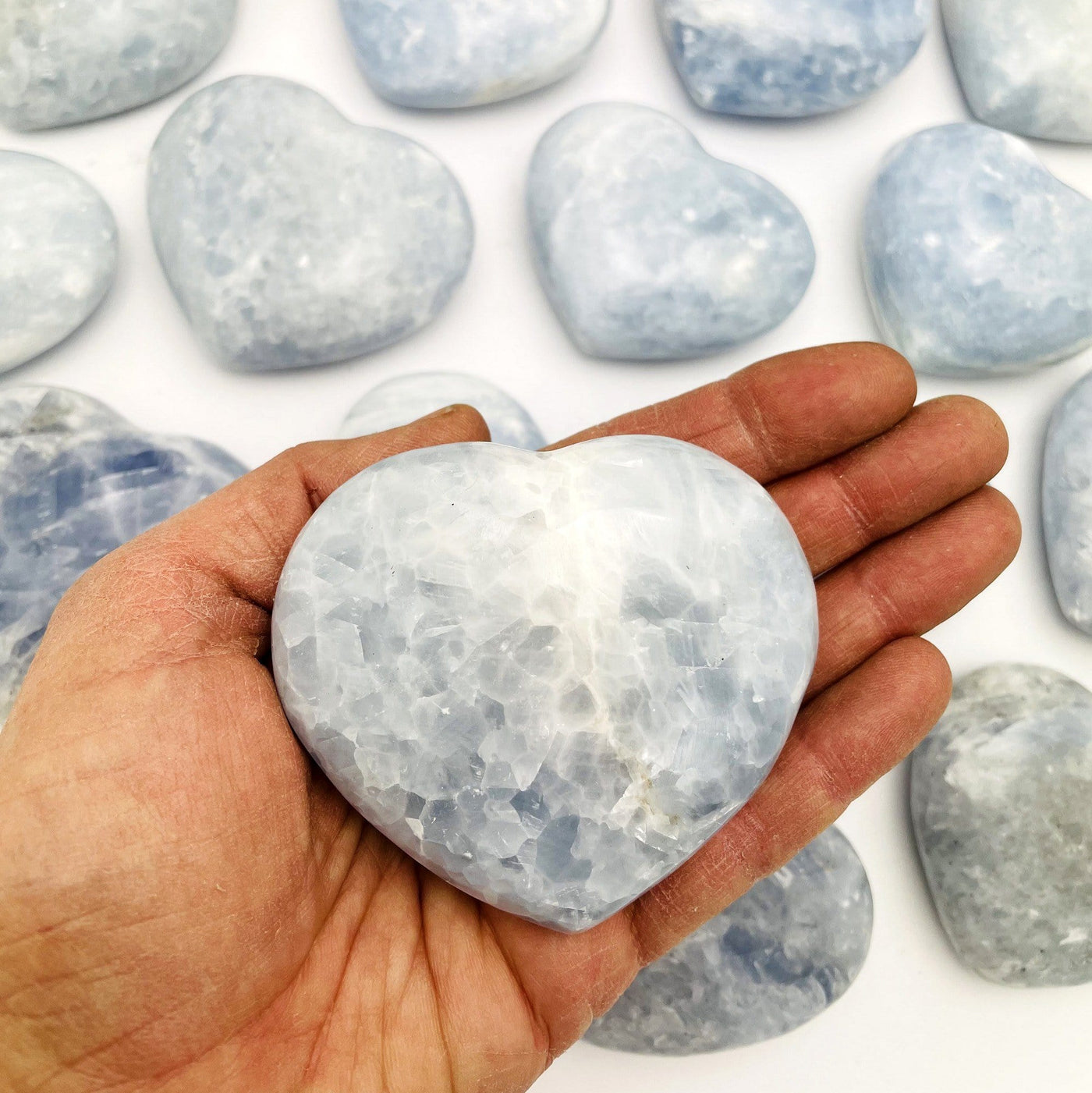 one Blue Calcite Heart in a hand and others behind on a table