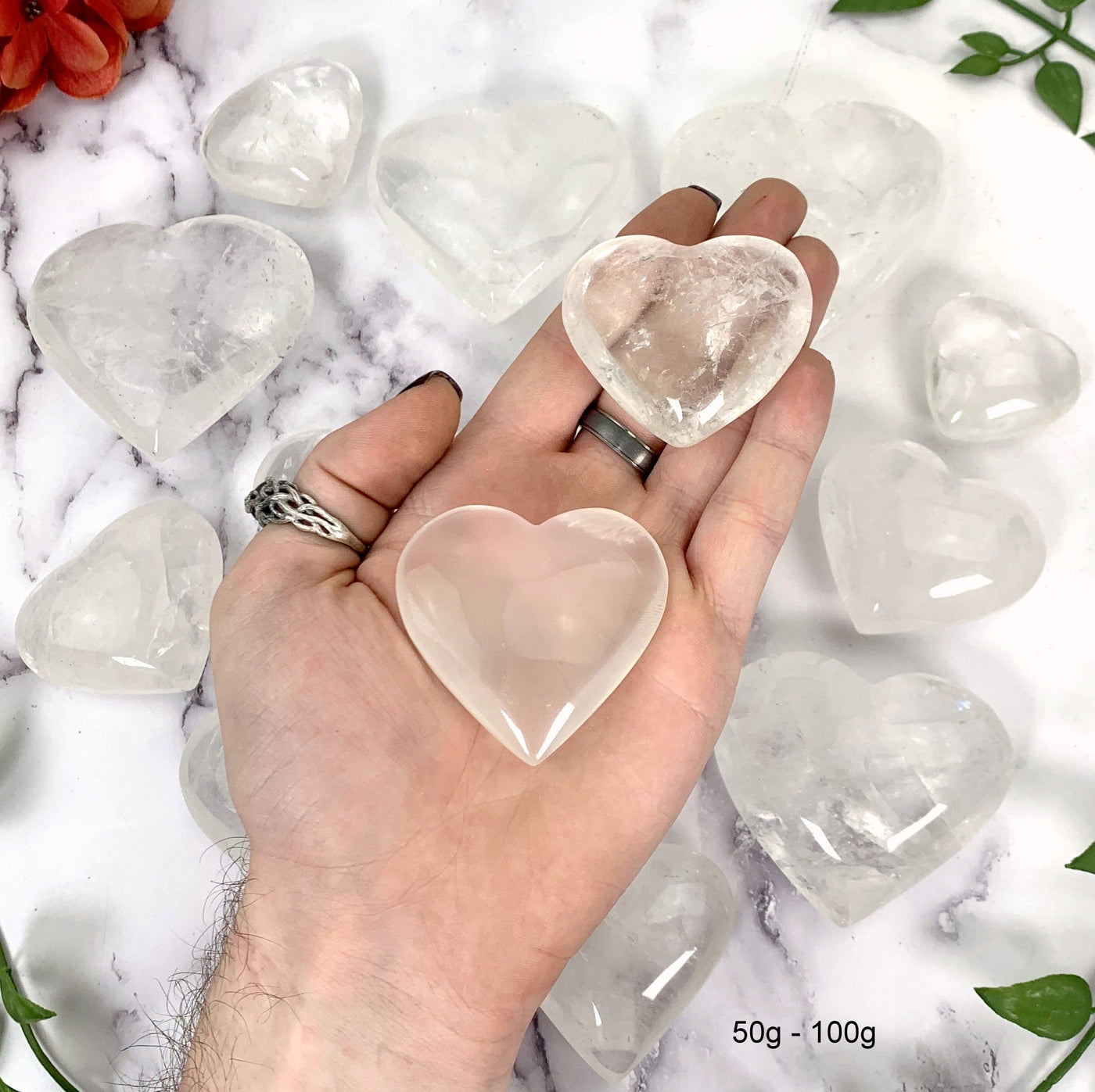Crystal Quartz Heart--2 50gram-100gram hearts in hand with multiple hearts in background. 