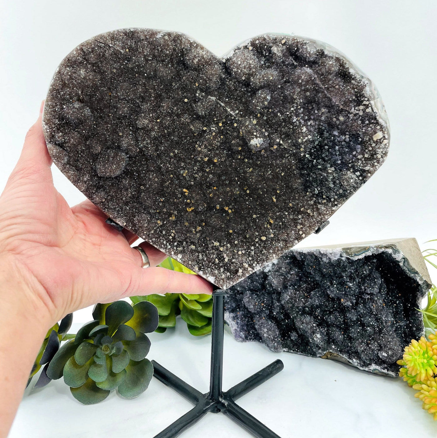 Dark Black Amethyst Heart on a metal stand with a hand touching it.