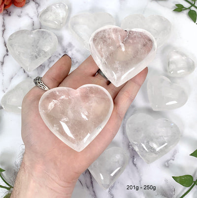 Crystal Quartz Heart--2 201gram-250gram hearts in hand with multiple hearts in background.