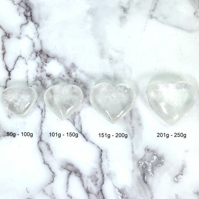 Crystal Quartz Heart--Top view of all 4 sizes of hearts laid out side by side on a marble background.