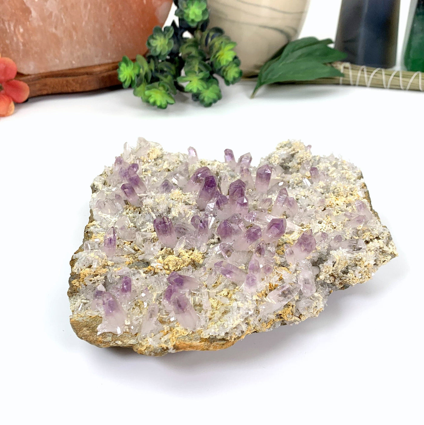 Veracruz amethyst cluster on white background.  It  light purple points scattered on a rock background that is tones of grey white and tan.  Tiny light purple points surround the large points.