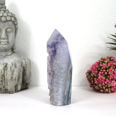side view of Dyed Amethyst crystal Polished tower with decorations in the background