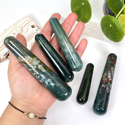 multiple bloodstone massage wands in hand displaying the different sizes and color patterns 