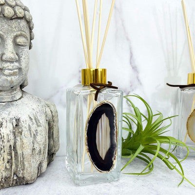 Picture of our black agate slice diffuser being displayed next to plants on a marbled background.