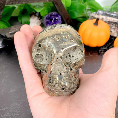 handholding up Pyrite Skull with decorations in the background