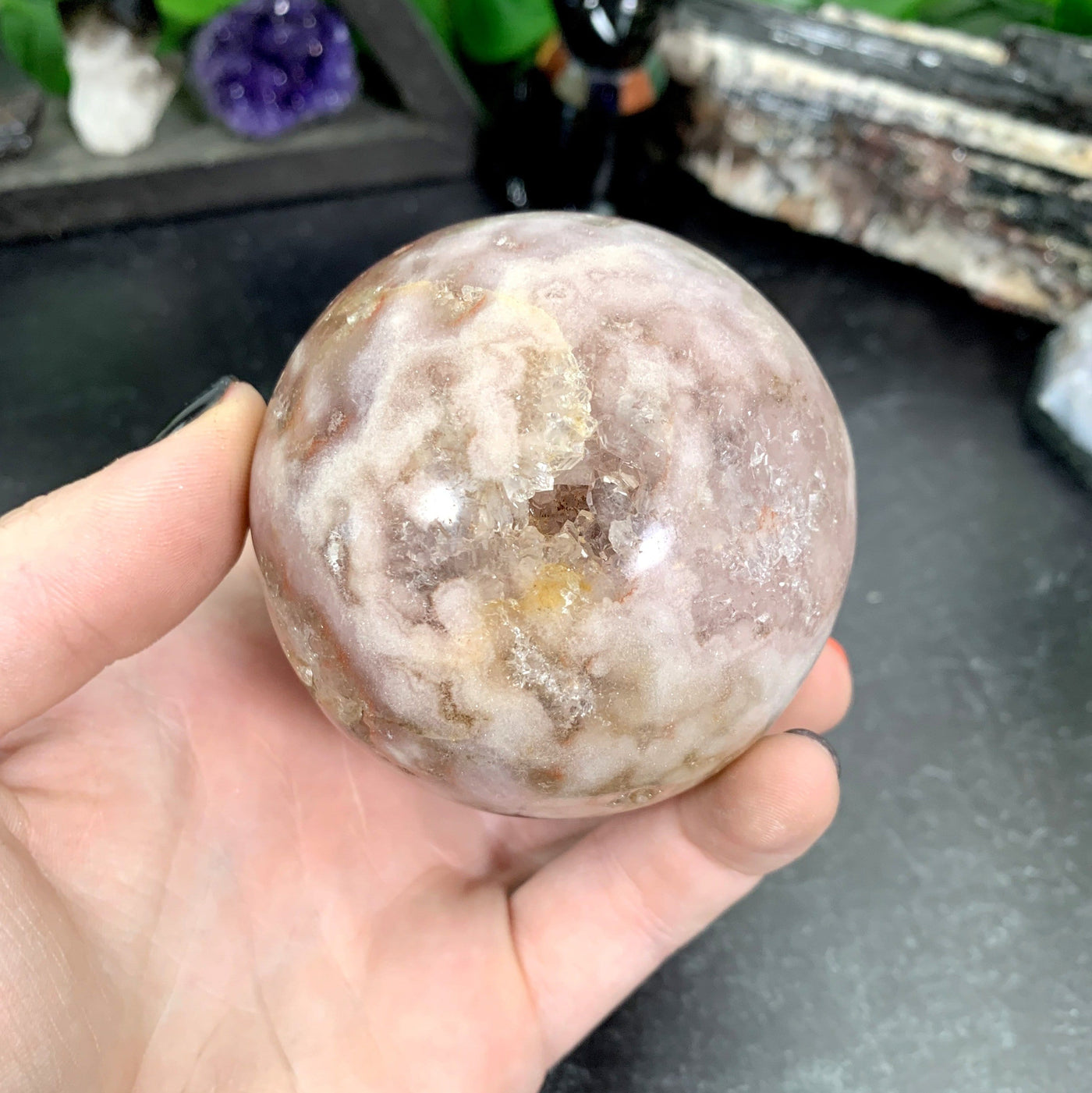 hand holding up Pink Amethyst Druzy Sphere with decorations in the background