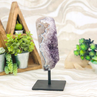 side view of Amethyst Crystal Purple Druzy Semi Polished Stalactite Geode on Stand with decorations in the background