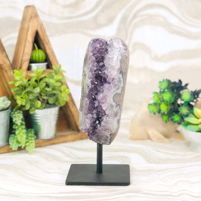 side view of Amethyst Crystal Purple Druzy Semi Polished Stalactite Geode on Stand with decorations in the background