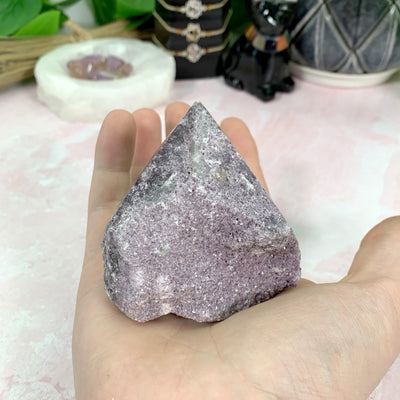 hand holding up Lepidolite Semi-Polished Point with decorations in the background