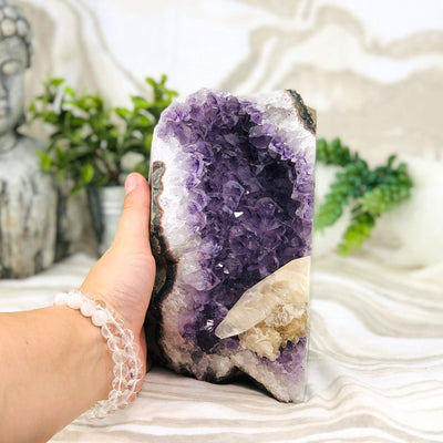hand next to Amethyst Cluster with Calcite with decorations in the background