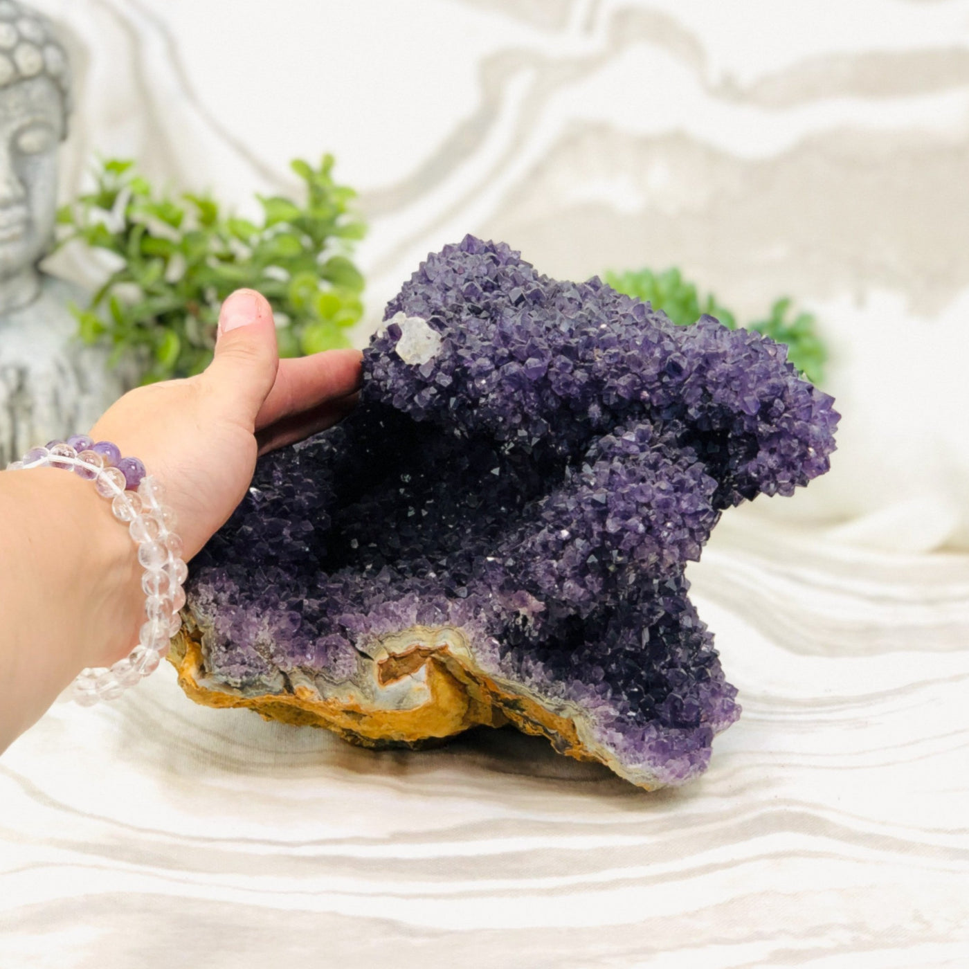 hand next to Amethyst Cluster Stalactite with decorations in the background