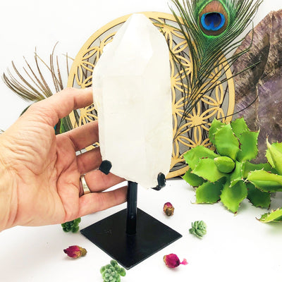 hand holding Crystal Quartz Point Stone on Metal Stand with decorations in the background