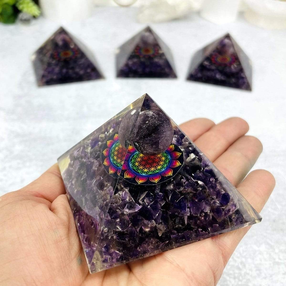 4 Orgone Amethyst Pyramids with Flower of Life Medallion, 1 up close in a hand and the others behind