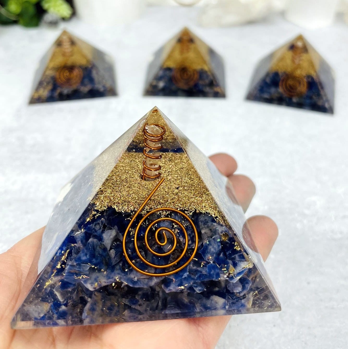 4 Orgone Sodalite with Crystal Point Pyramid displayed, 3 out of focus and 1 in focus, held in hand.