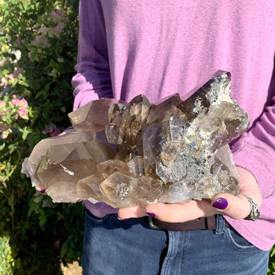 smoky rutilated quartz in hands with pink shirt and floral background