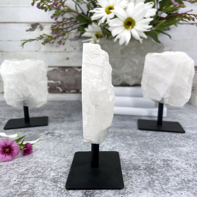 A side view of One Polished Crystal Quartz Stone on Metal Stand and 2 in the Background 