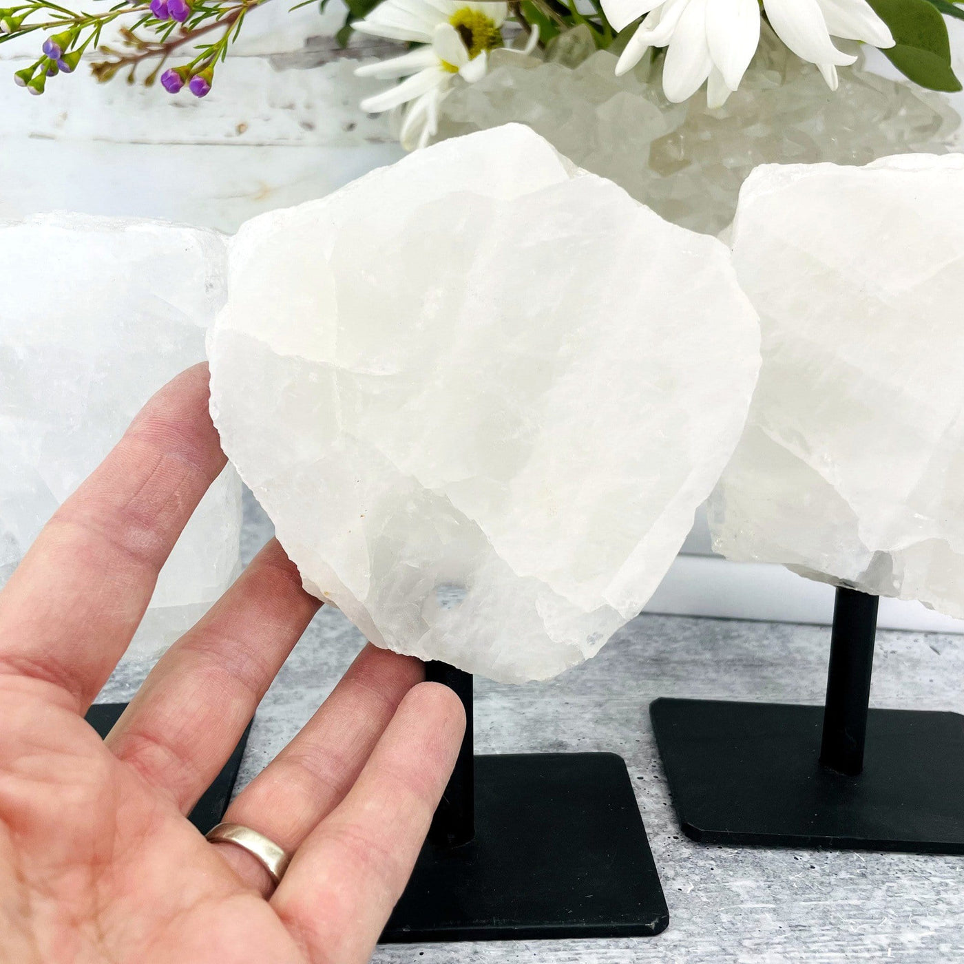 Hand Touching 1 Polished Crystal Quartz Stone on Metal Stand  with 2 in the background 