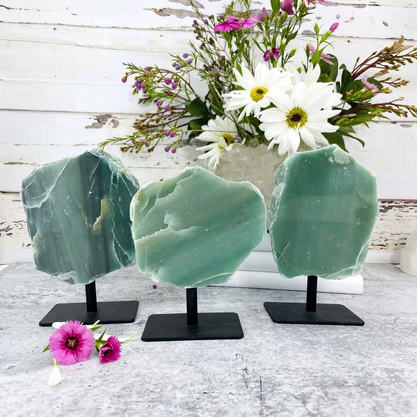 3 polished green quartz on metal stands with flowers in the background