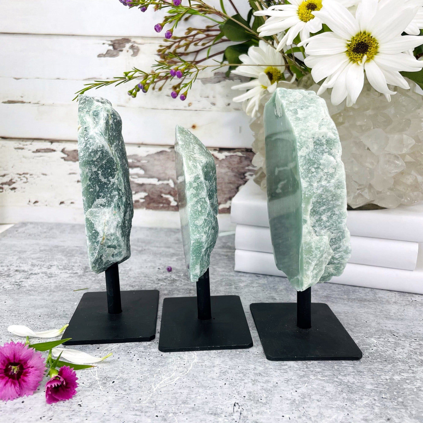 side view of 3 polished green quartz on metal stands with flowers in the background