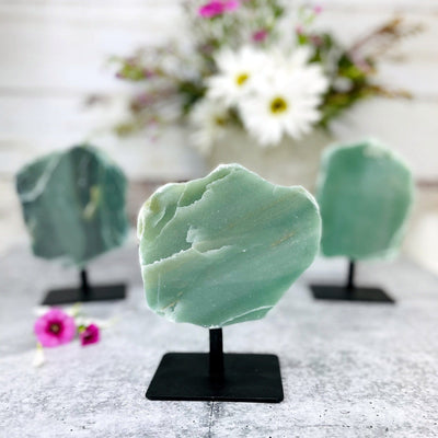 up close shot of polished green quartz on metal stand with 2 others blurred in the background