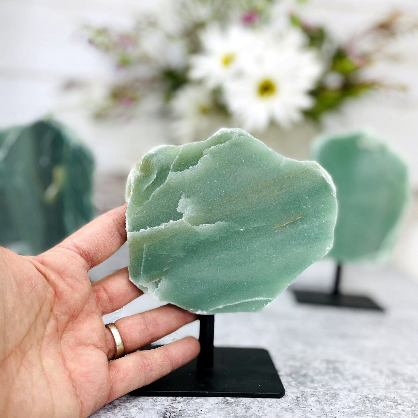 hand holding up polished green quartz on metal stand with 2 others blurred in the background