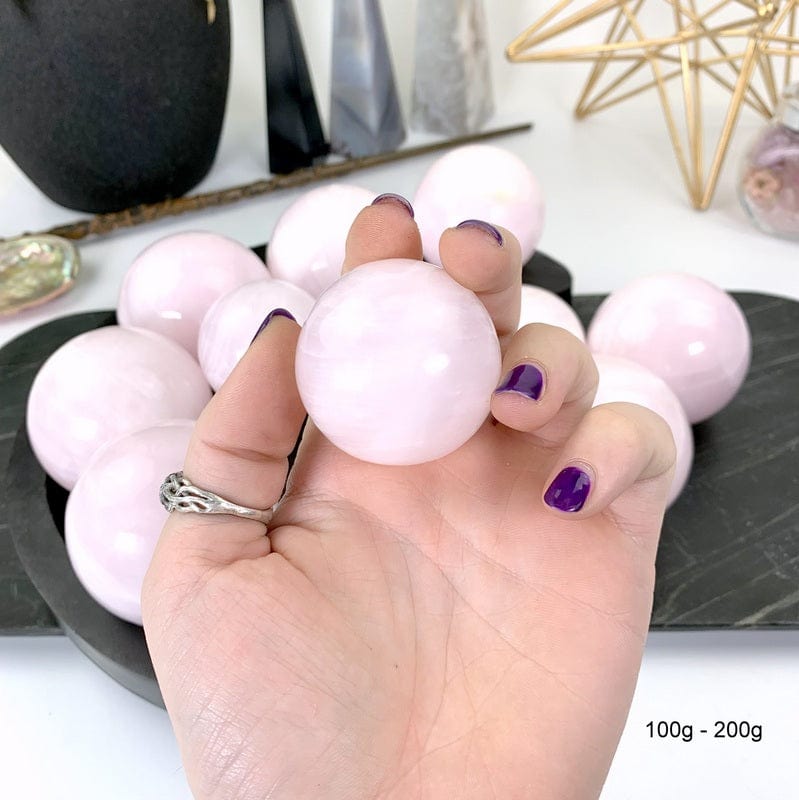 100 gram - 200 gram pink calcite sphere in hand with white background