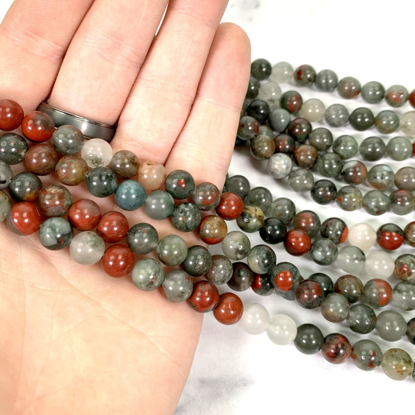 Close up of African Bloodstone Polished Round Beads on Strand in a hand.