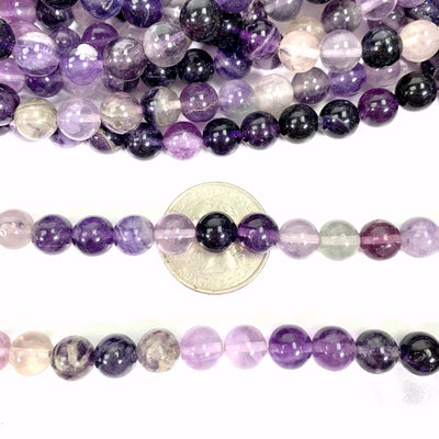 purple fluorite beads laying across a quarter on a white background
