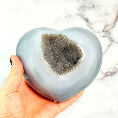 Druzy Natural Agate Heart Shaped Stone in a hand with a light colored background.