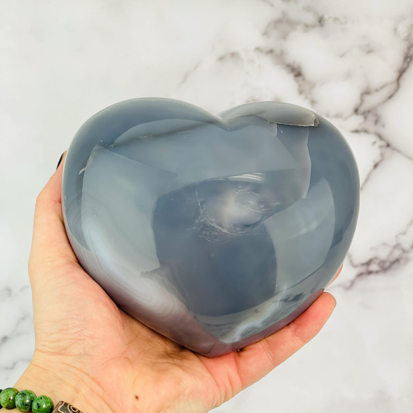 Backside of agate heart in a hand showing the polished external surface.