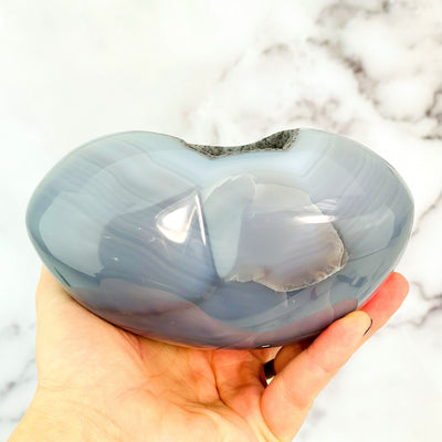 Bottom view of agate heart within a hand to show product thickness.