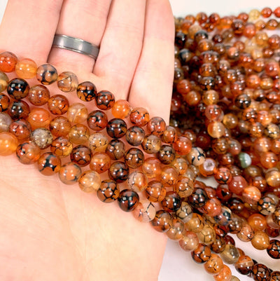 red polished agate beads in hand with more beads in the background